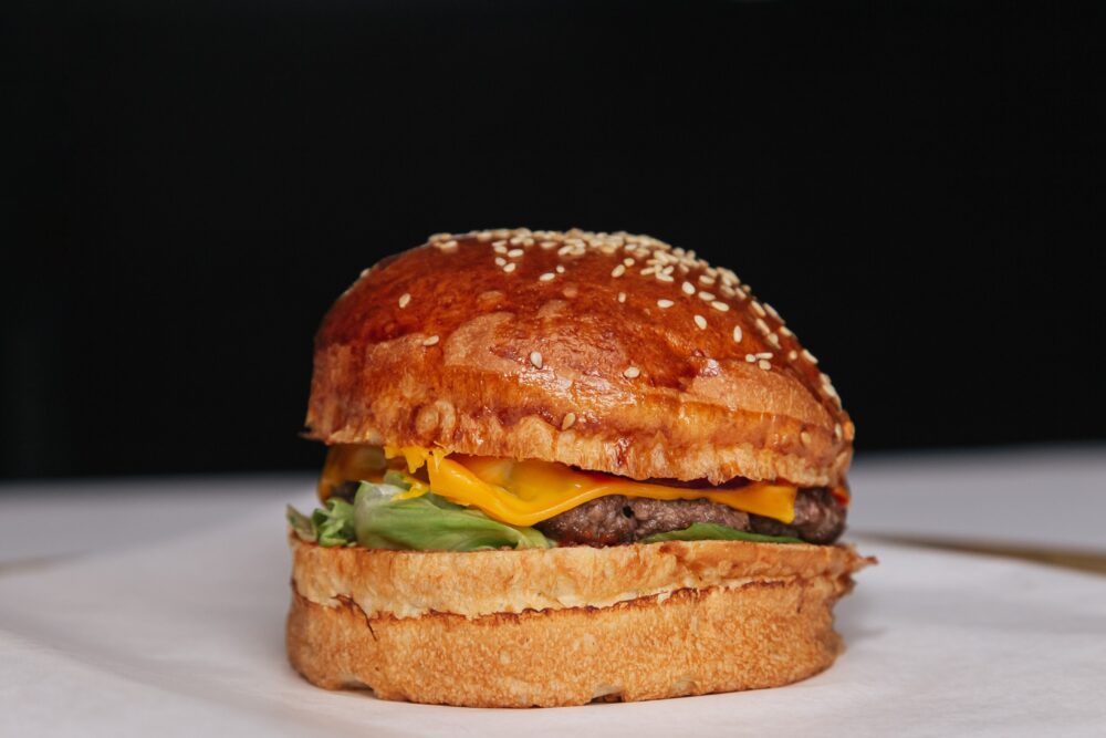 A cheeseburger with lettuce and sesame bun on white surface.