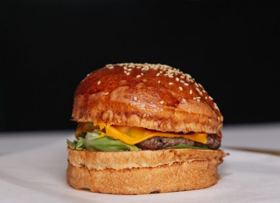 A cheeseburger with lettuce and sesame bun on white surface.