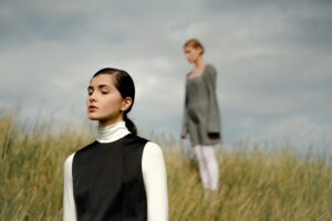 Two people stand in a grassy field under cloudy sky.