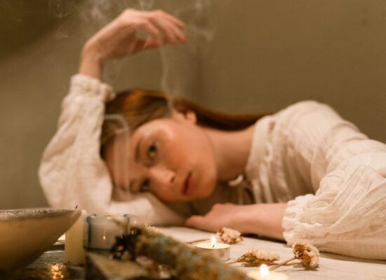 Person resting head on table with candles and dried flowers.