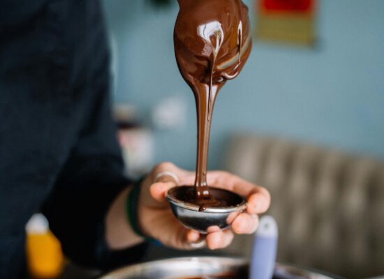 Person pouring melted chocolate into a small mold, kitchen setting.