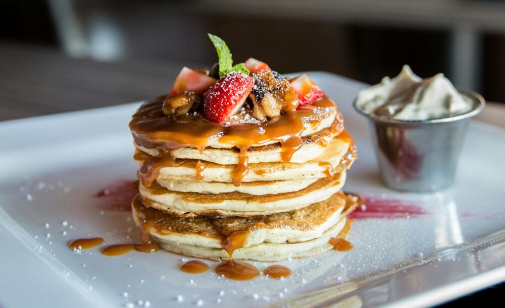 Stack of pancakes with caramel, strawberries, and whipped cream.