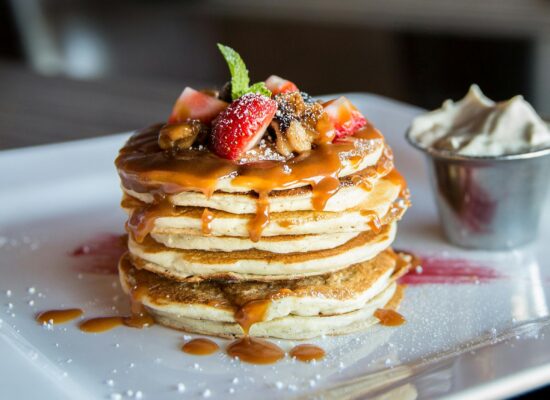 Stack of pancakes with caramel, strawberries, and whipped cream.