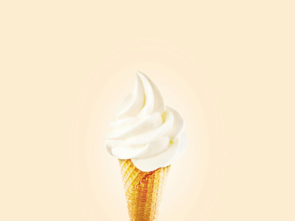 Vanilla soft serve ice cream cone on a plain background.