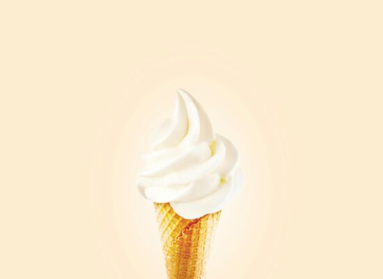 Vanilla soft serve ice cream cone on a plain background.