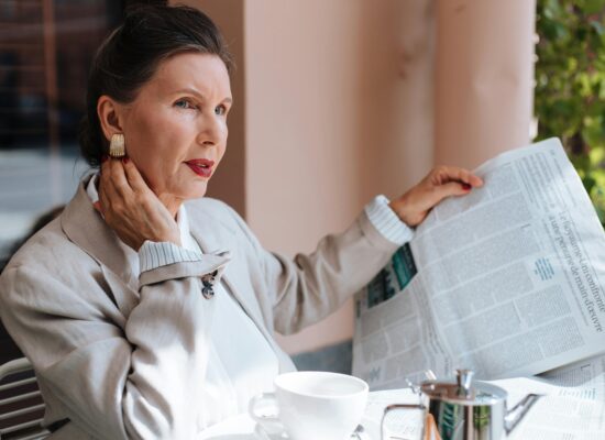 Person sitting at table, reading newspaper, drinking coffee, looking thoughtful.