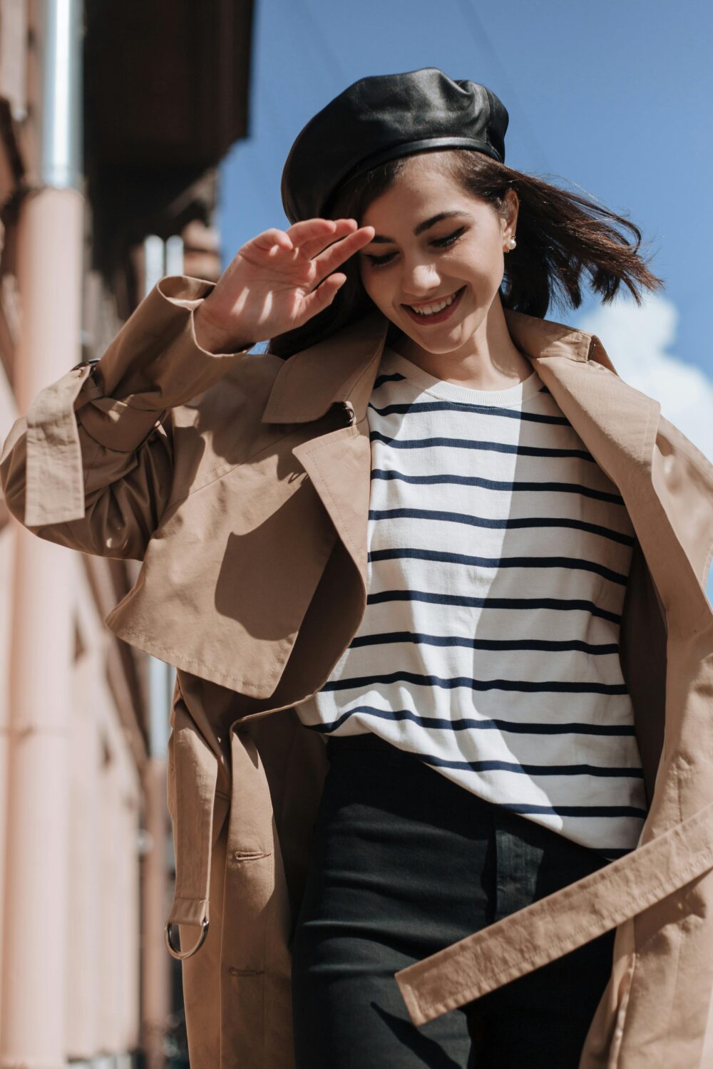 Person smiling outdoors, wearing trench coat and striped shirt.