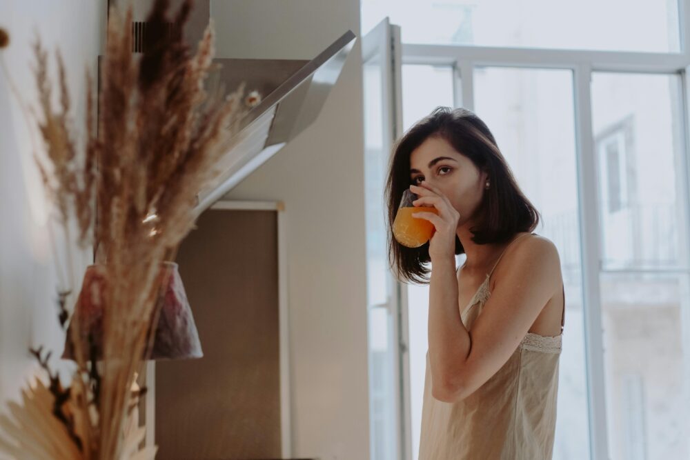 Person in a kitchen drinks orange juice, morning light shines in.