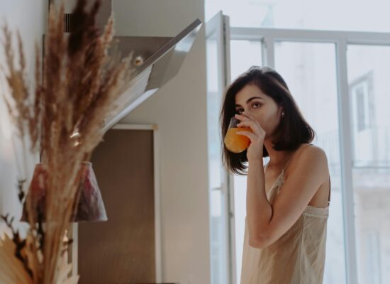 Person in a kitchen drinks orange juice, morning light shines in.