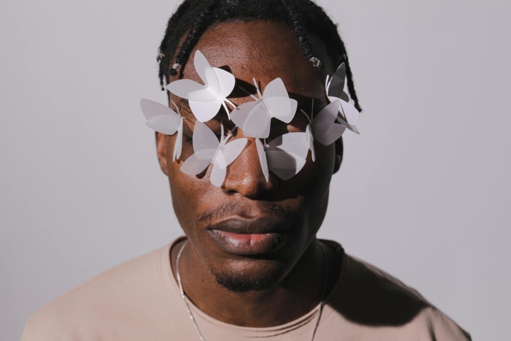 Person with paper butterflies on face, neutral background, artistic style.