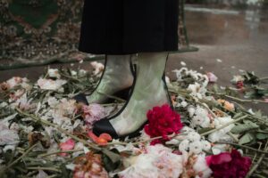 A person stands in a pile of flowers wearing clear boots.