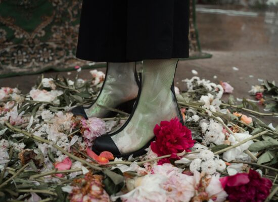 A person stands in a pile of flowers wearing clear boots.