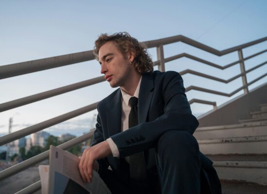 A person in a suit sits on stairs holding a newspaper.