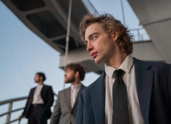 Three men in suits stand under a bridge looking out.