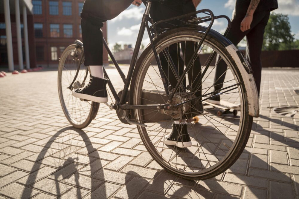 Close-up of a person on a bicycle with a skateboard nearby.