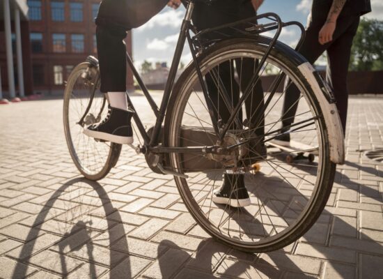 Close-up of a person on a bicycle with a skateboard nearby.