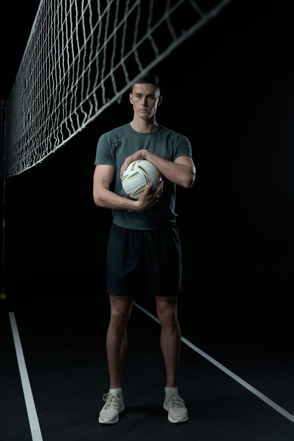 Person standing on volleyball court holding a volleyball, dark background.