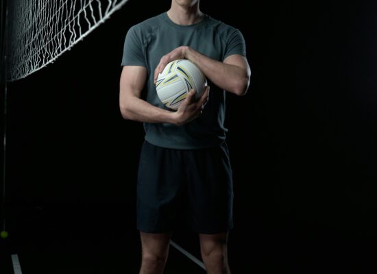 Person standing on volleyball court holding a volleyball, dark background.
