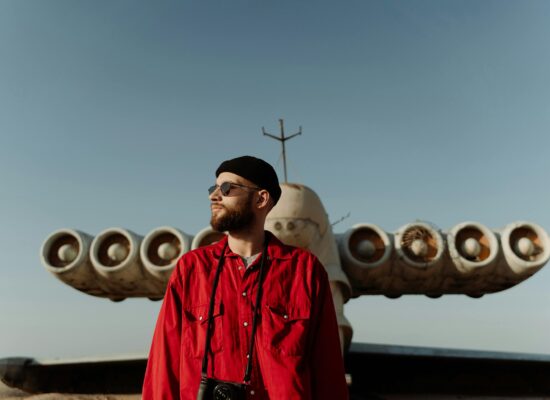 Person in red shirt stands before large, unusual aircraft outdoors.