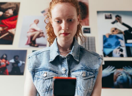 Person looking at phone with photos on wall behind them.