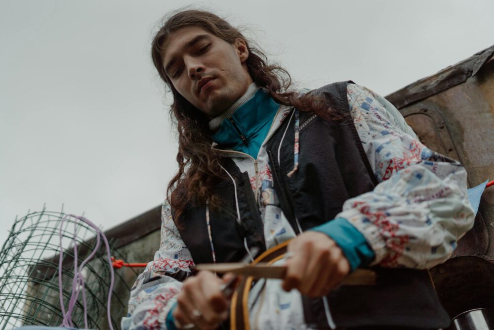 A person with long hair wearing a patterned jacket and blue collar.