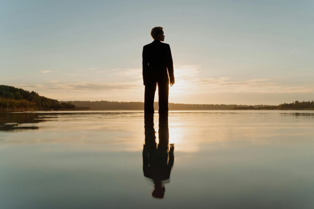 Silhouette of a person standing in calm water at sunset.