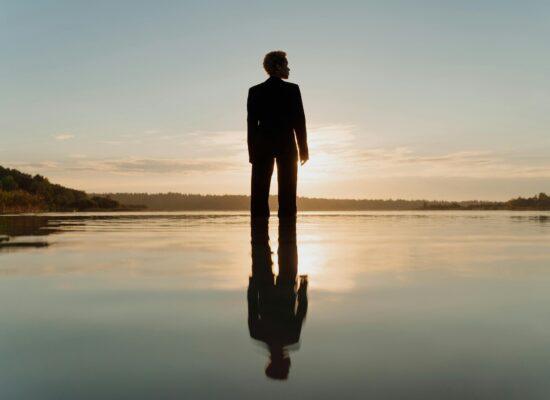 Silhouette of a person standing in calm water at sunset.