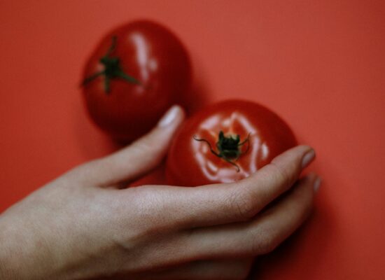 A hand holding a tomato, another tomato on red background.