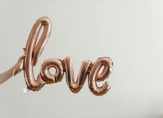 Rose gold balloon spelling 'love' held against plain background.