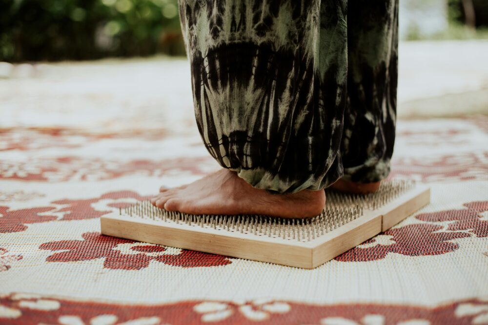 Person standing barefoot on a bed of nails, patterned mat underneath.