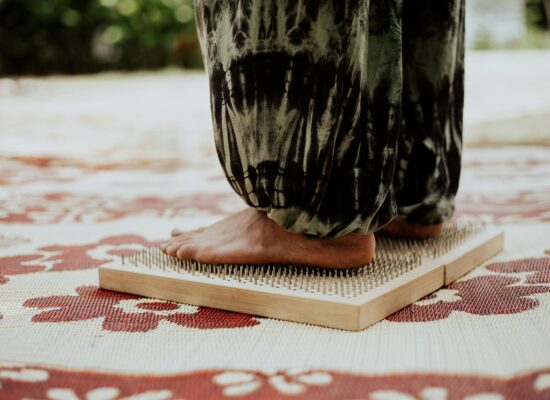 Person standing barefoot on a bed of nails, patterned mat underneath.