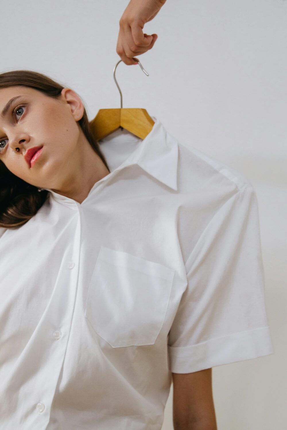 Person in white shirt with hanger, head tilted sideways.