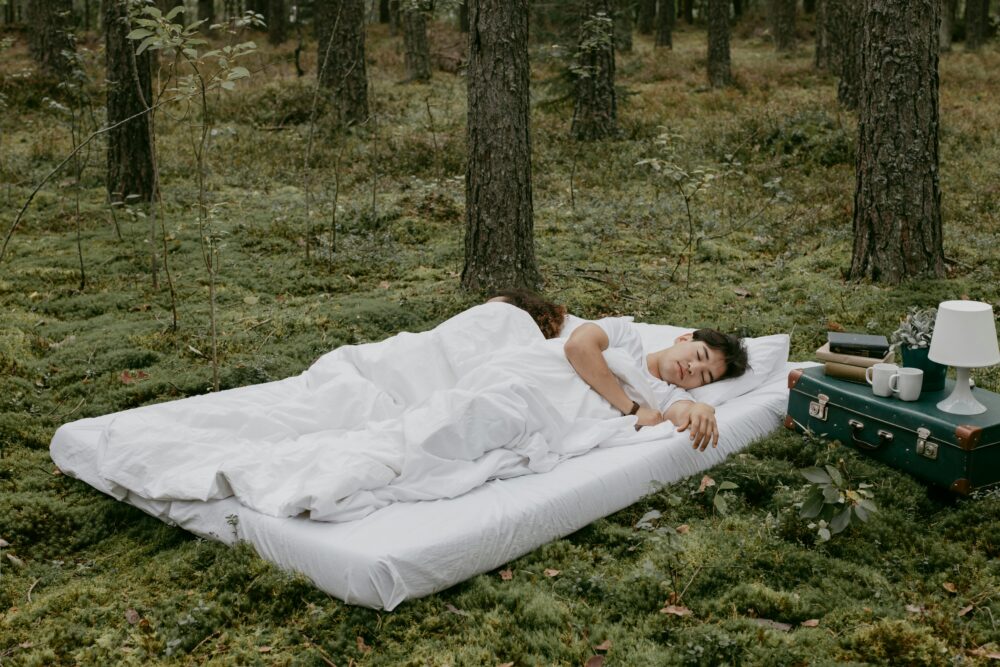 Two people sleeping on a bed in a forest setting.