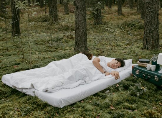 Two people sleeping on a bed in a forest setting.