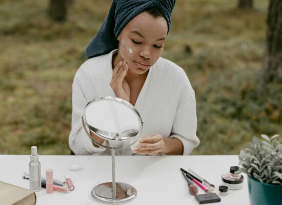 Person applying skincare at a table with beauty products outdoors.