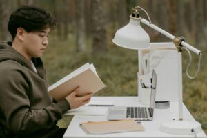 Person reading a book at a desk outdoors, studying.