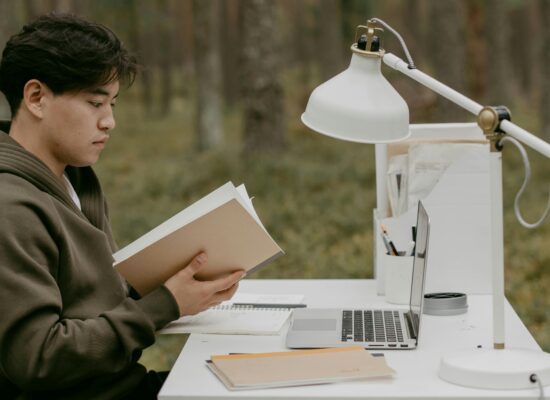 Person reading a book at a desk outdoors, studying.