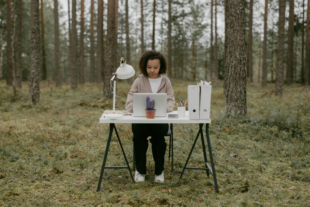 Person working at a desk with laptop in forest setting.