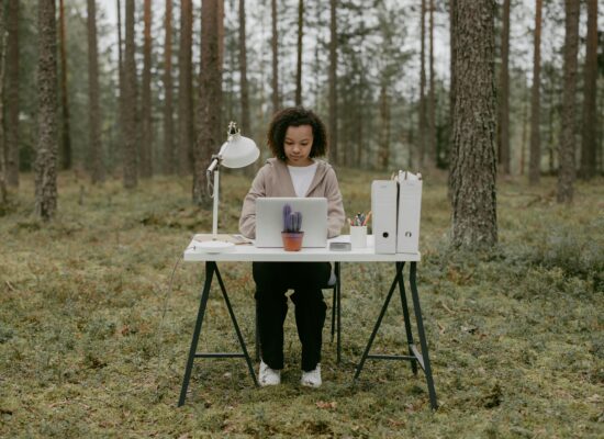Person working at a desk with laptop in forest setting.