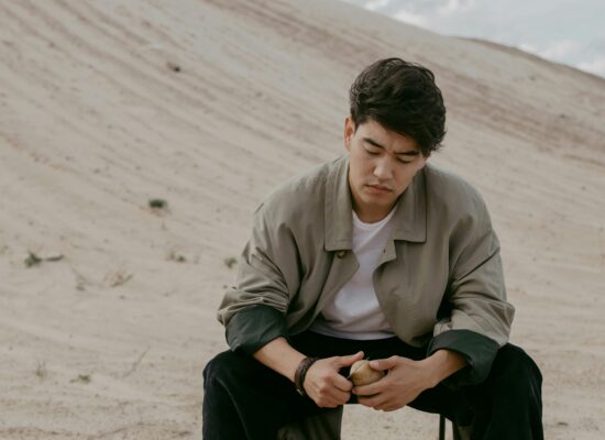 Person sitting on sand, peeling a potato, looking thoughtful.