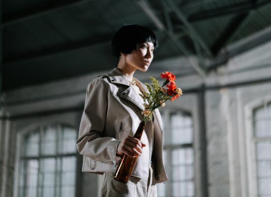 Person in light jacket holding flowers in a brown bottle.