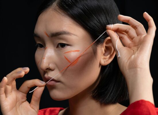 Person with face paint holding string near face, black background.