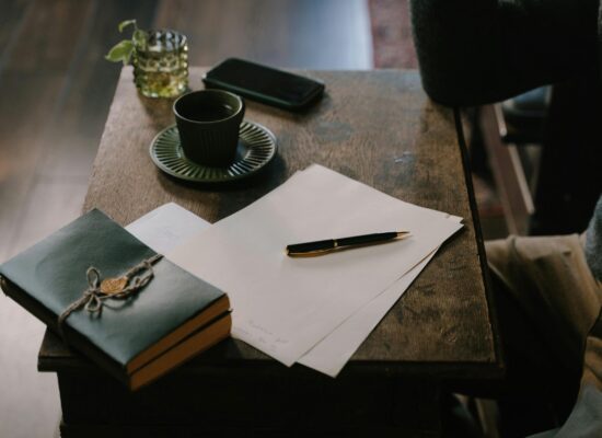 Notebook, pen, papers, coffee, and phone on wooden table.