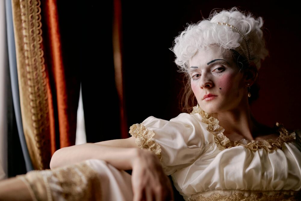 Person in historical costume with white wig and dramatic makeup.