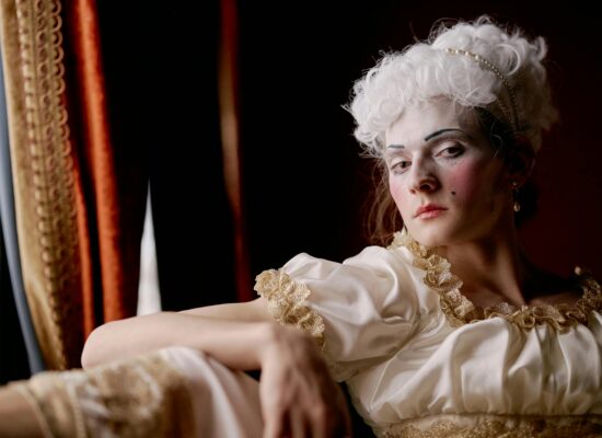 Person in historical costume with white wig and dramatic makeup.