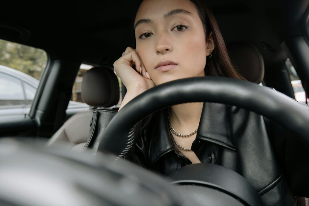 Person sitting in a car, looking thoughtful behind steering wheel.