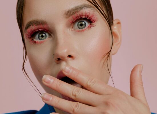 Person with surprised expression, pink makeup, hand near mouth.