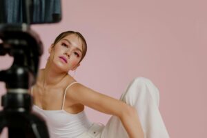 Person posing in front of camera with pink background, makeup.