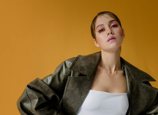 Person in stylish jacket poses against solid yellow background, confident.