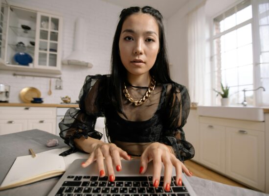 Person typing on laptop in bright kitchen, notebook nearby.